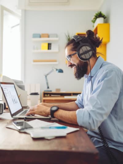 Person with beard and headphones works on a laptop.